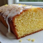 Close-up of a slice of moist lemon pound cake topped with thick white glaze and lemon zest.