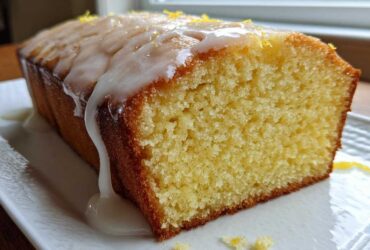 Close-up of a slice of moist lemon pound cake topped with thick white glaze and lemon zest.