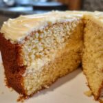 Close-up of a moist slice of vanilla cake recipe showing the fluffy crumb and creamy frosting.
