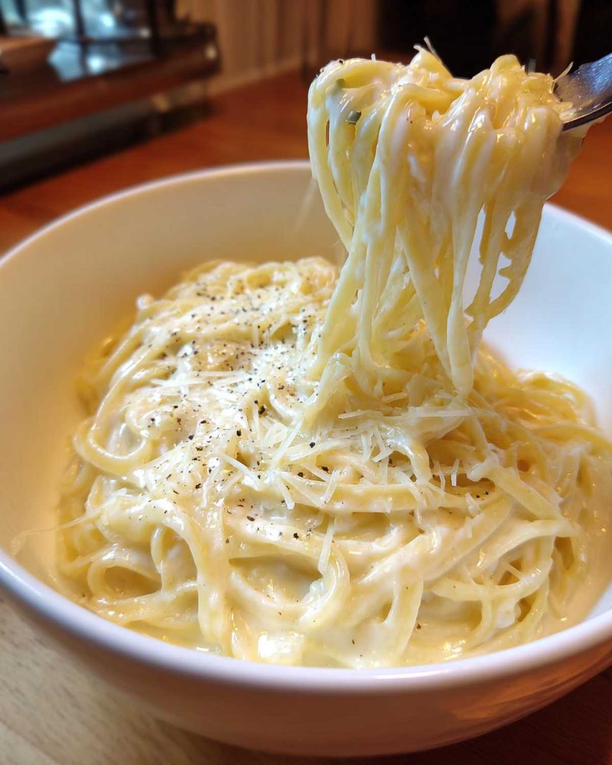 A fork lifts creamy fettuccine coated in rich Olive Garden Alfredo Sauce, topped with grated Parmesan and black pepper.