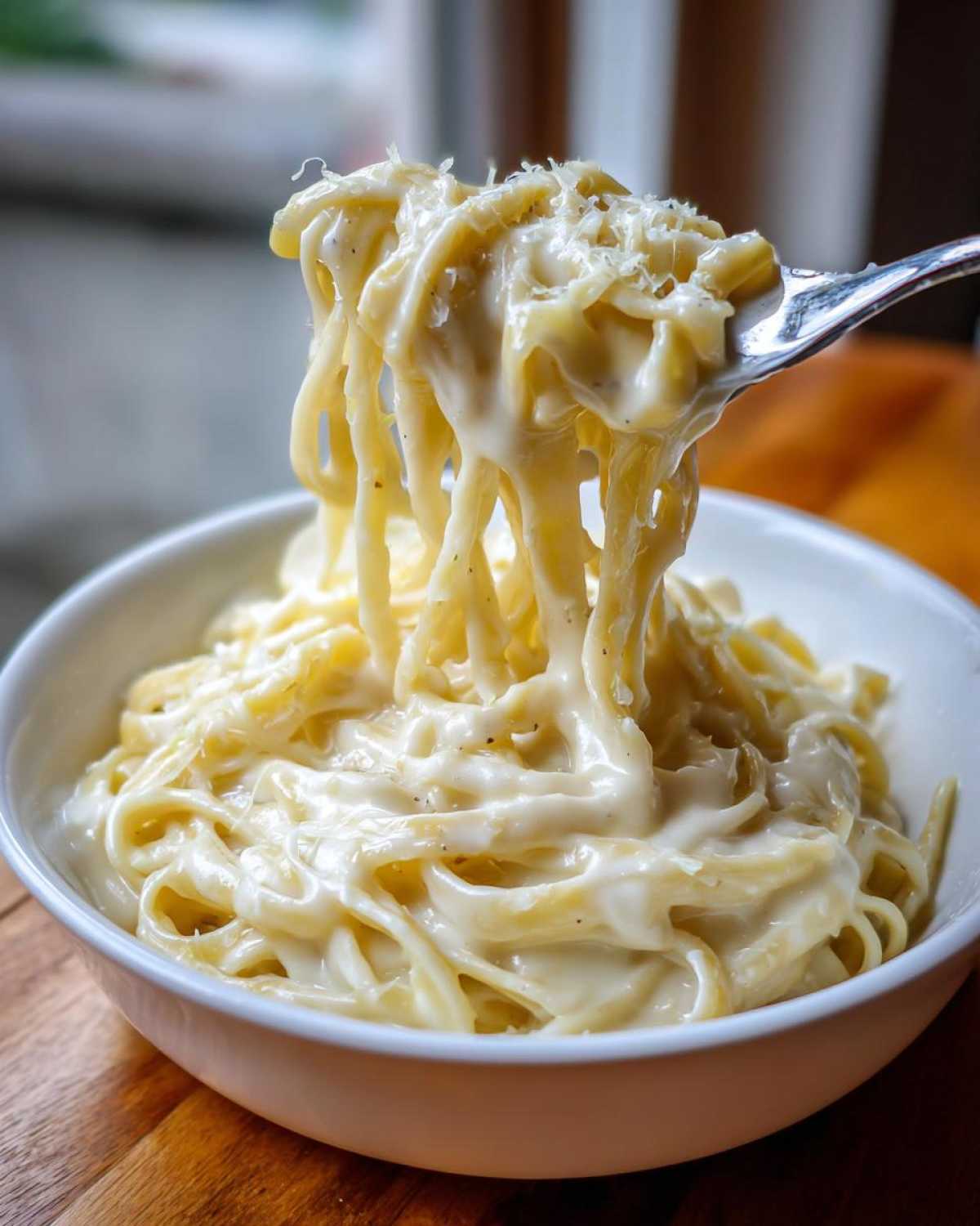 A fork lifting creamy fettuccine coated in rich Olive Garden Alfredo sauce, topped with grated Parmesan.