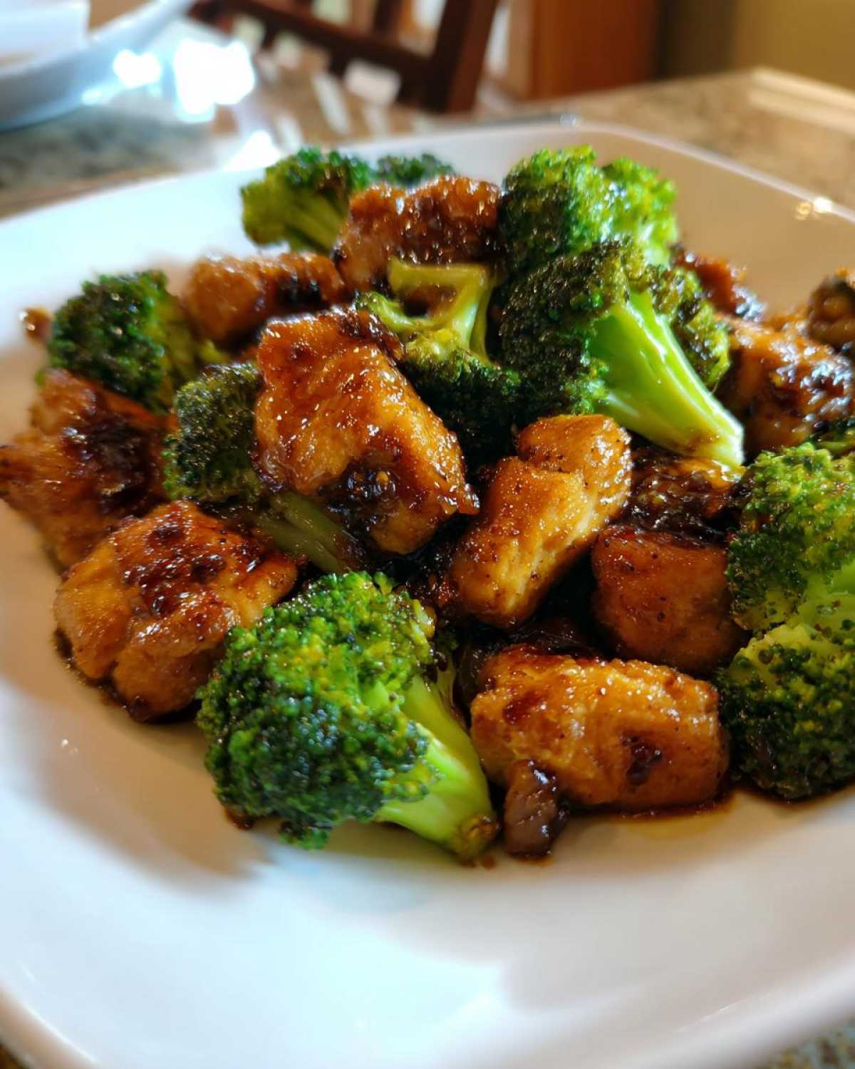 Close-up of bite-sized chicken pieces coated in a dark sauce mixed with bright green broccoli florets, featuring chicken and broccoli.