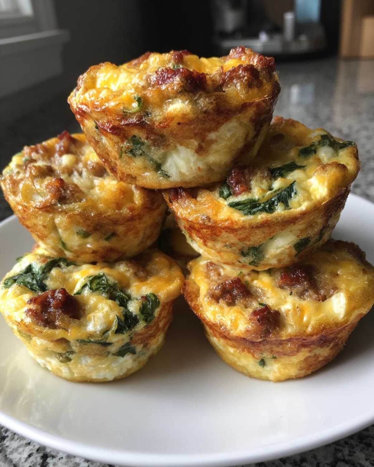A stack of five golden-brown Egg Muffin Cups filled with visible pieces of sausage, spinach, and melted cheese.