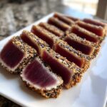 Slices of perfectly cooked Seared Ahi Tuna, crusted with black and white sesame seeds, arranged on a white platter.