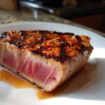Close-up of a perfectly seared tuna steak, rare in the center, resting in its juices after using the MARINADE FOR TUNA STEAK.