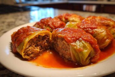 Close-up of several cabbage rolls topped with bright red tomato sauce, one cut open showing the meat and rice filling.