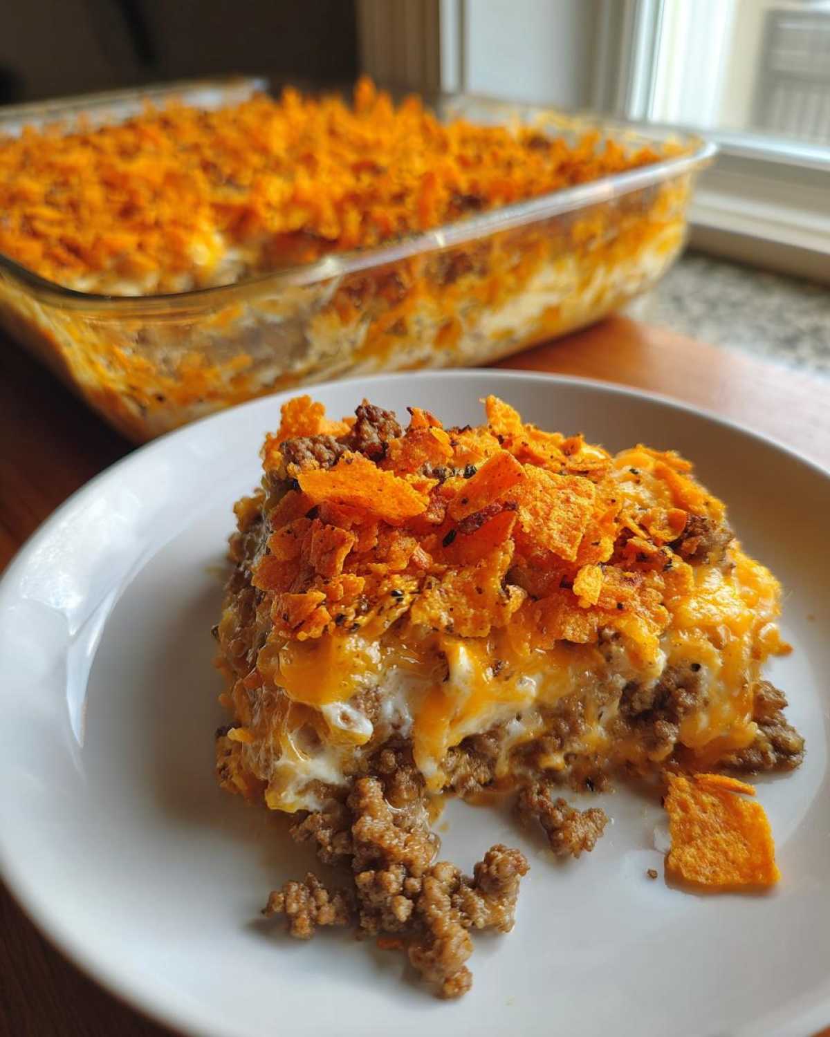 A serving of creamy Dorito Casserole topped with melted cheese and crushed Doritos on a white plate.