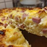 Close-up of a creamy slice being lifted from a baked scalloped potatoes and ham dish, showing melted cheese and diced ham.