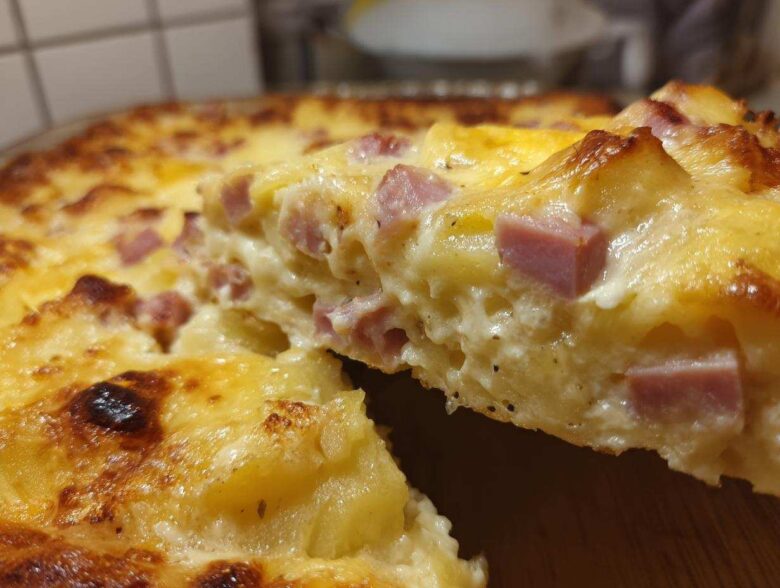 Close-up of a creamy slice being lifted from a baked scalloped potatoes and ham dish, showing melted cheese and diced ham.