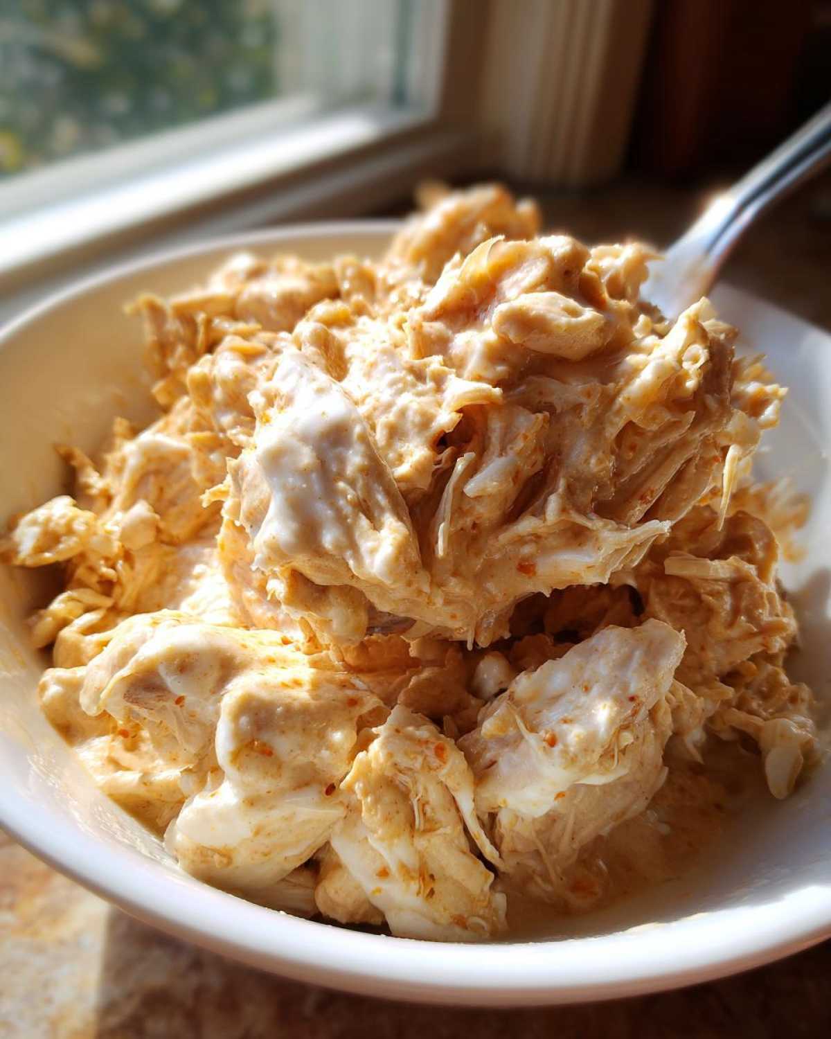 Close-up of shredded chicken coated in a creamy, spiced sauce, ready for crockpot white chicken chili.