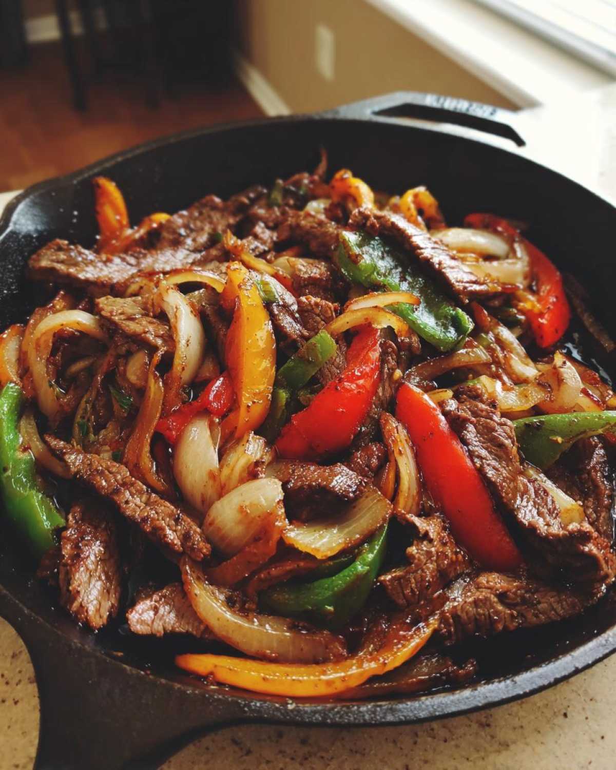 Close-up of sizzling steak fajitas with colorful bell peppers and onions served in a black cast iron skillet.
