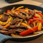 Close-up of sizzling steak fajitas with colorful bell peppers and onions served in a black cast iron skillet.