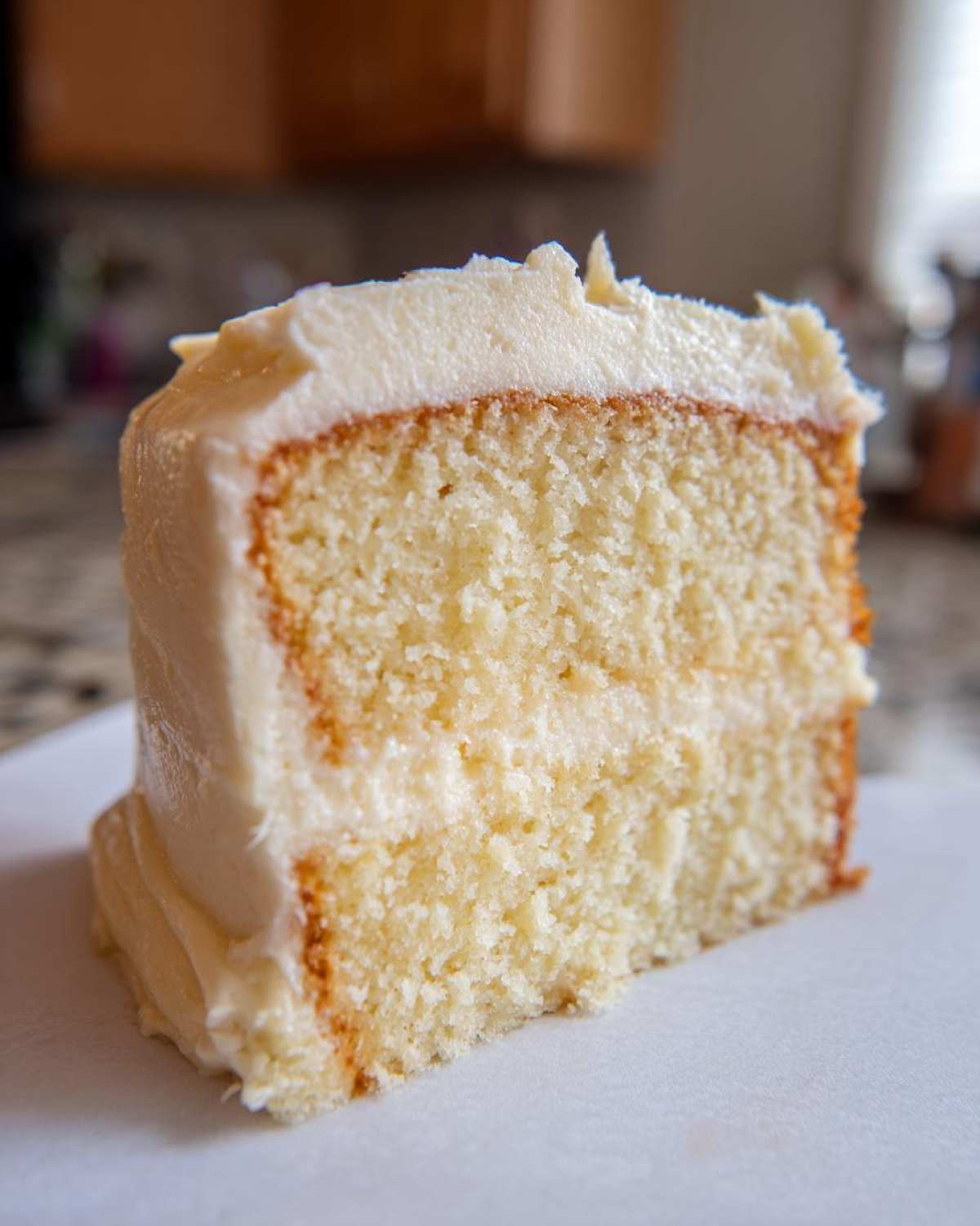 Close-up of a thick slice of moist vanilla cake recipe layered with creamy white frosting.