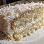 Close-up of a moist slice of coconut cake with white frosting and shredded coconut topping.