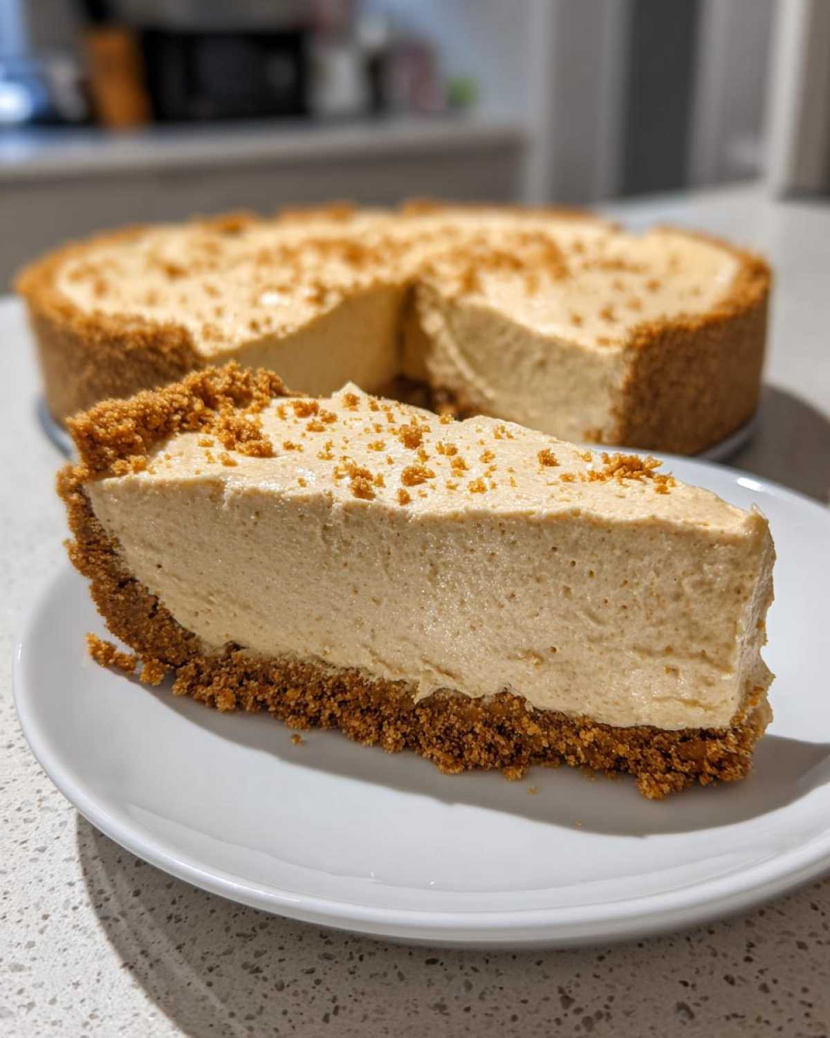 A thick slice of creamy peanut butter pie with a graham cracker crust sits on a white plate.