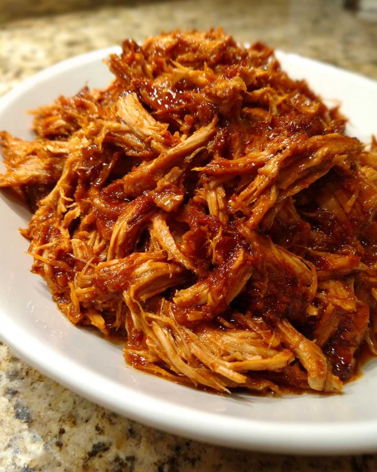 A close-up shot of shredded, saucy Slow Cooker Pulled Pork piled high in a white bowl.