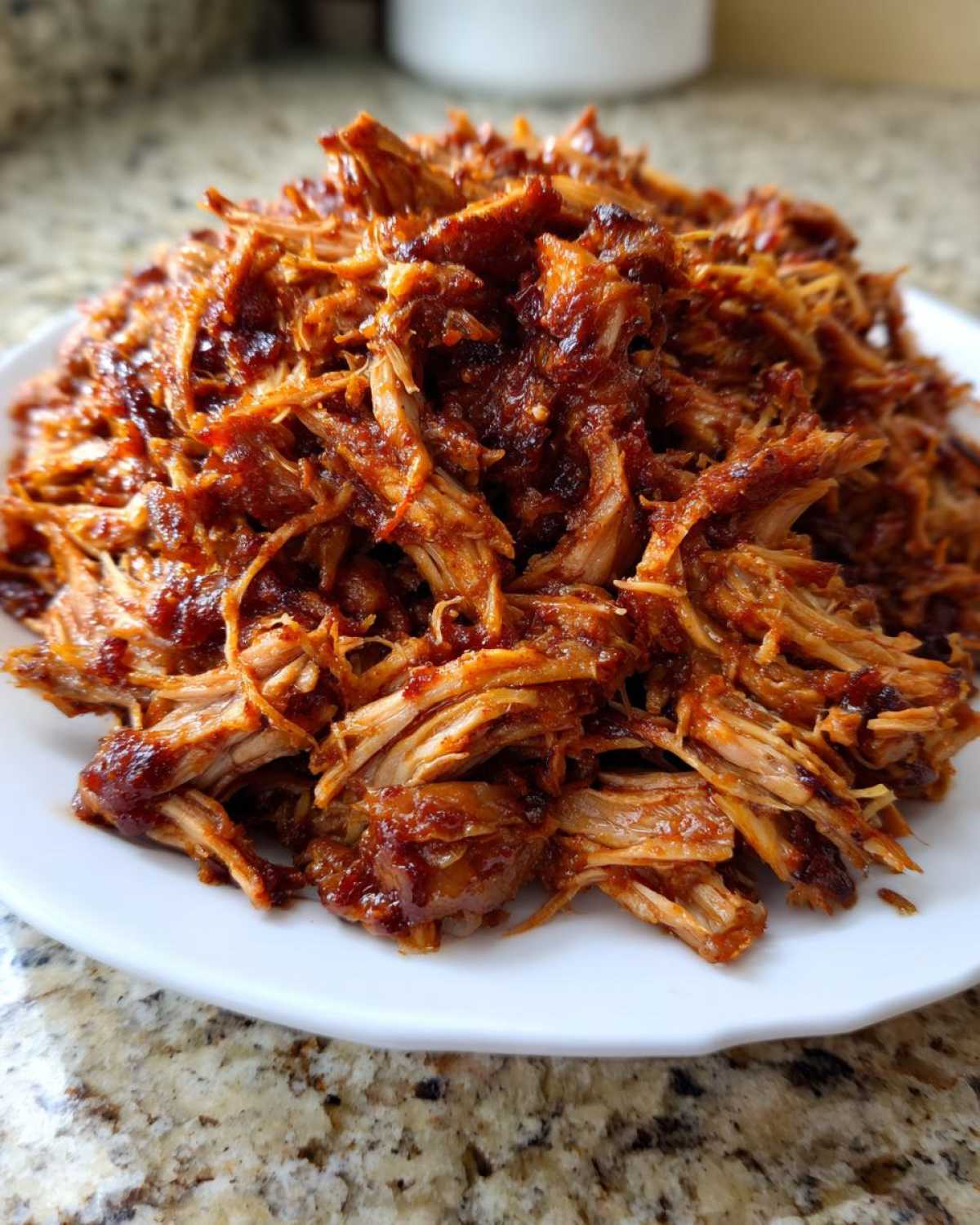 A close-up of shredded, saucy Slow Cooker Pulled Pork piled high on a white plate.