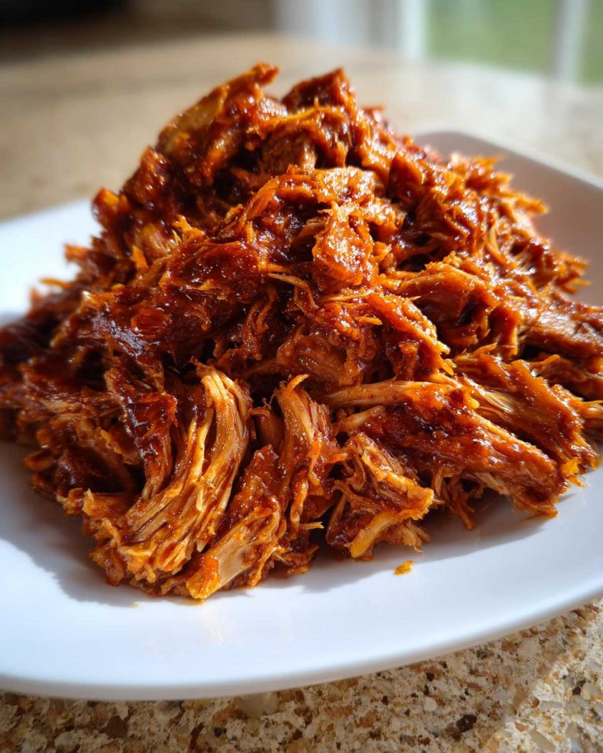 Close-up of shredded, saucy Slow Cooker Pulled Pork piled high on a white plate.