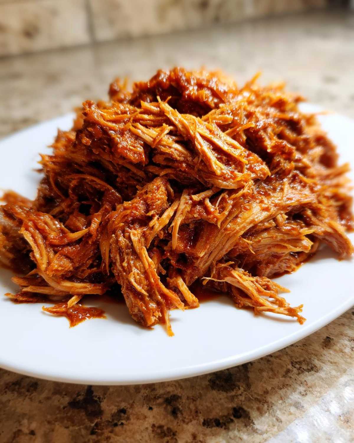 A close-up of tender, saucy Slow Cooker Pulled Pork, shredded and piled high on a white plate.