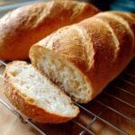 Close-up of a freshly baked french bread loaf with one slice cut, showing the soft, airy interior crumb.