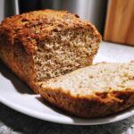 Close-up of a freshly baked loaf of soft whole wheat bread with one slice cut, revealing the dense crumb.