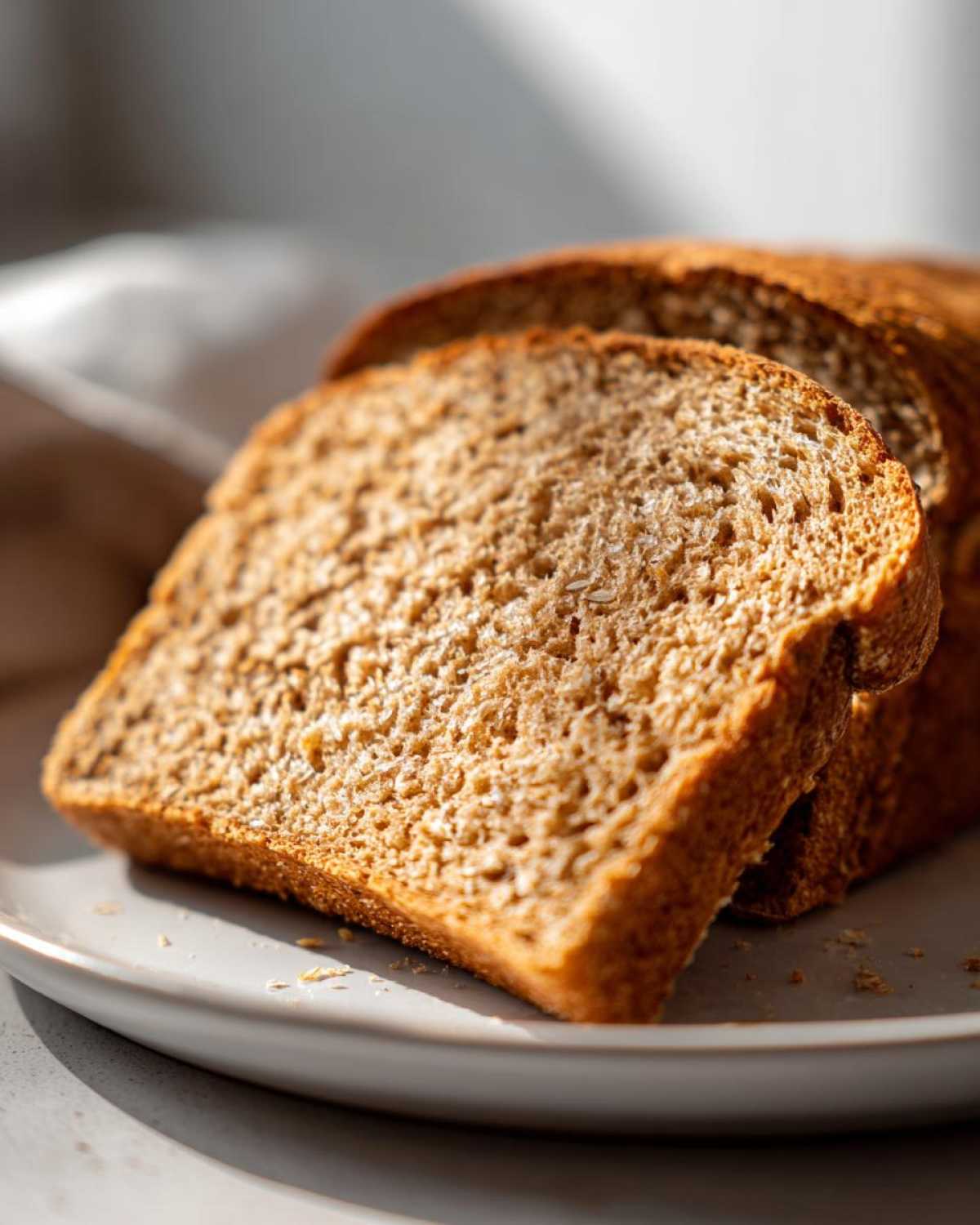 Close-up of two thick slices of soft whole wheat bread resting on a light gray plate.