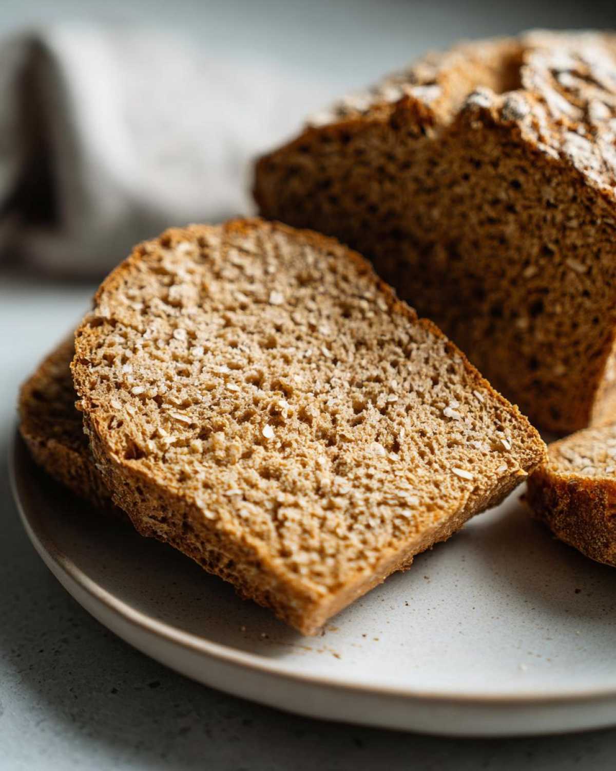 Close-up of thick slices of soft whole wheat bread showing the texture and grains on a speckled plate.