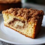 Close-up of a moist slice of sour cream coffee cake featuring a cinnamon swirl and thick streusel topping.