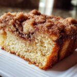 Close-up of a moist slice of sour cream coffee cake featuring a thick, sugary cinnamon crumb topping.
