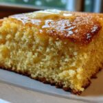 A close-up shot of a thick slice of golden sourdough cornbread topped with melting butter.