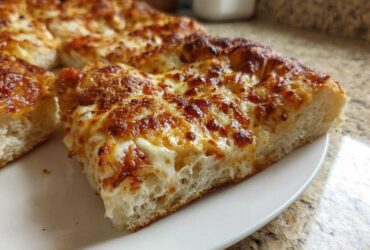 Close-up of a thick slice of cheesy pizza made with sourdough discard pizza dough, showing a fluffy crust.