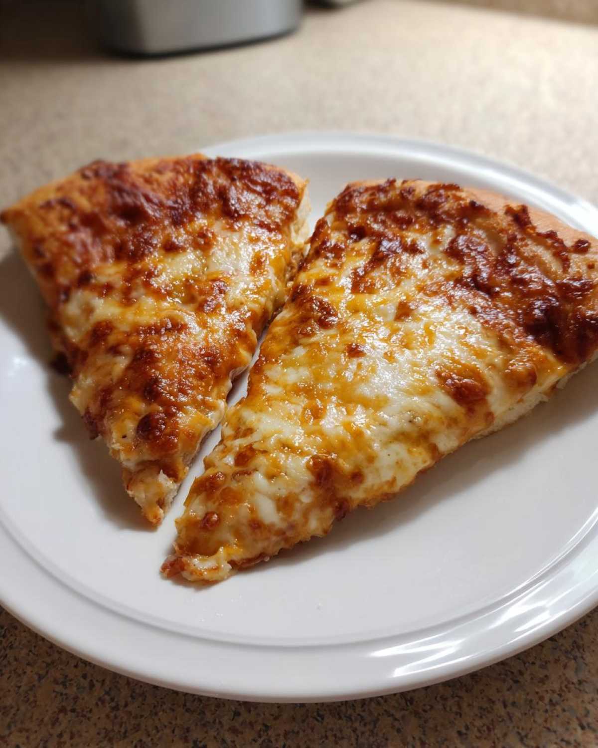 Two slices of cheesy pizza, made from sourdough discard pizza dough, served on a white plate.