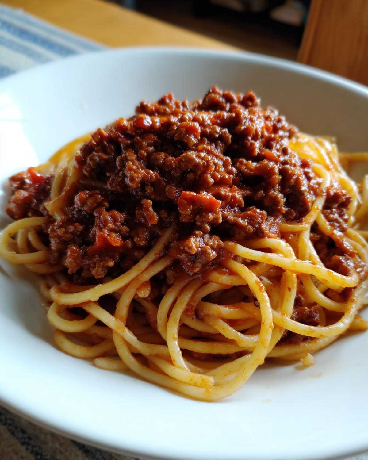 Close-up of spaghetti noodles generously topped with rich, dark red bolognese sauce in a white bowl.
