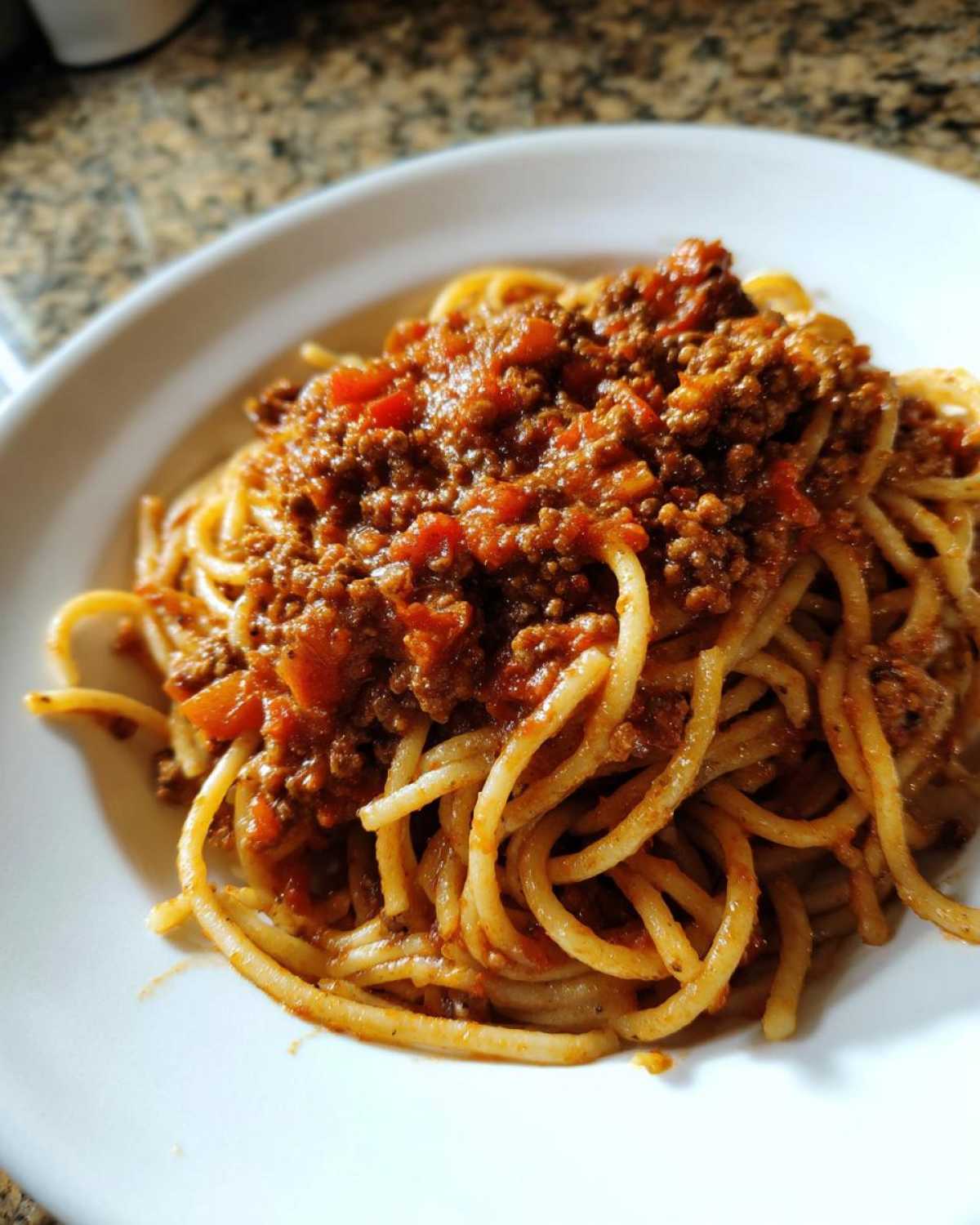 Close-up of spaghetti topped generously with rich, meaty bolognese sauce served on a white plate.