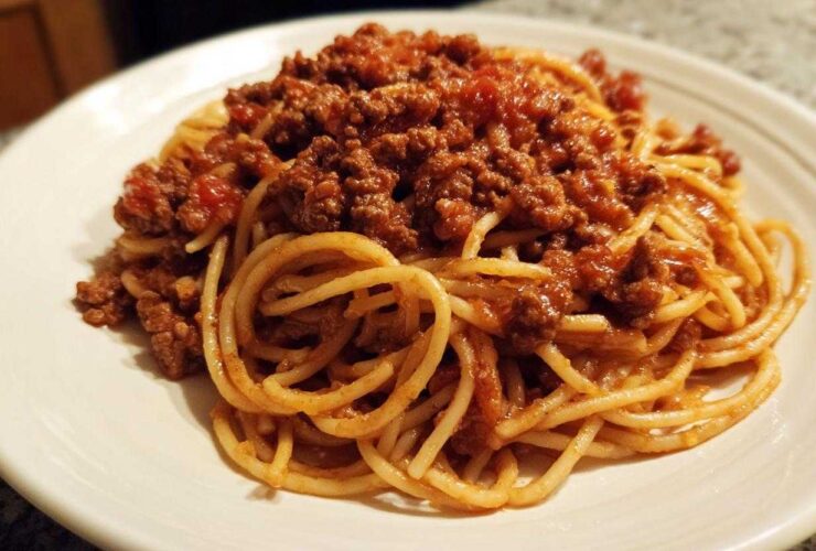 Close-up of spaghetti noodles generously topped with rich, meaty bolognese sauce on a white plate.