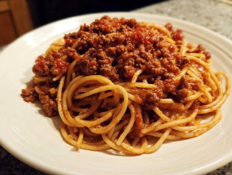 Close-up of spaghetti noodles generously topped with rich, meaty bolognese sauce on a white plate.