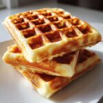A stack of three golden brown, freshly made high protein waffles resting on a white plate.
