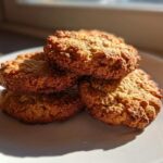 A small stack of four golden brown, textured oatmeal cookie treats resting on a white plate.
