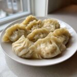 A plate of freshly steamed Traditional Chinese Dumplings with crimped edges, set near a window.