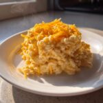 A serving of creamy, steaming hot cheesy rice topped generously with bright orange shredded cheddar cheese.