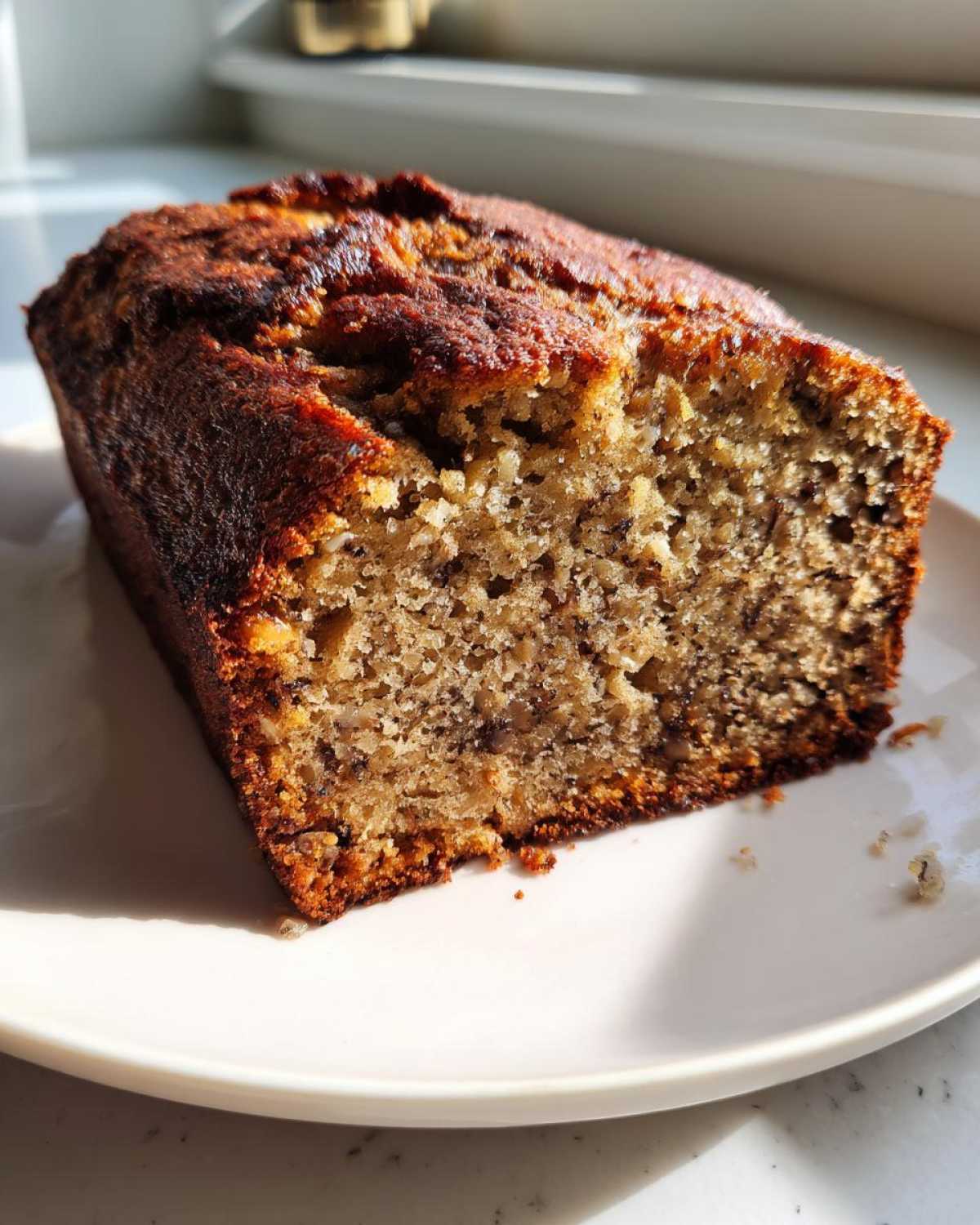 A close-up view of a slice of moist sugar free banana bread with a dark, caramelized crust.