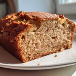 Close-up of a thick slice of moist sugar free banana bread with a golden brown crust, sitting on a white plate.
