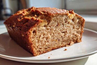 Close-up of a thick slice of moist sugar free banana bread with a golden brown crust, sitting on a white plate.