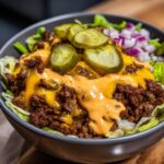 A close-up, tempting shot of a cheeseburger bowl featuring seasoned ground beef, melted cheese, special sauce, pickles, and diced onions.