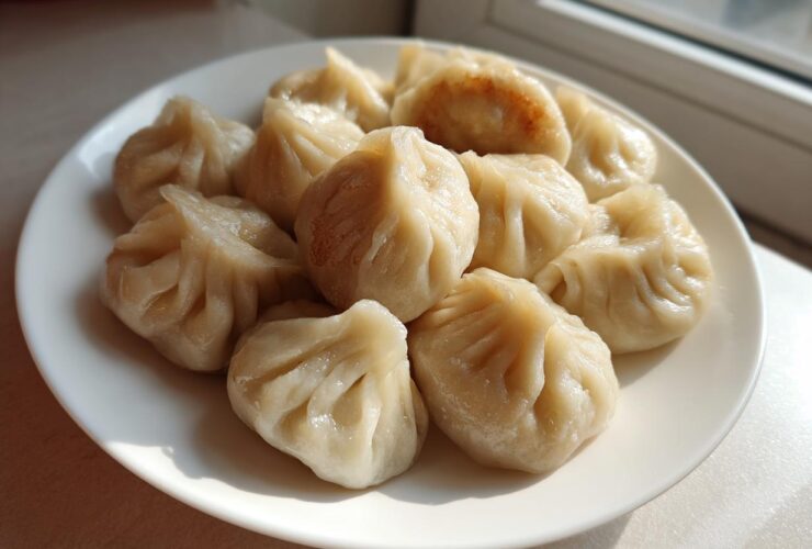 A plate filled with freshly steamed Traditional Chinese Dumplings, showing pleated wrappers and one slightly pan-fried dumpling.