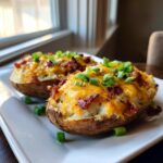 Two perfectly prepared twice baked potatoes loaded with melted cheddar cheese, bacon bits, and fresh green onions.