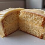 Cross-section of a moist vanilla cake recipe slice showing the fluffy crumb and thick layer of pale yellow frosting.