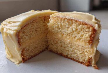Cross-section of a moist vanilla cake recipe slice showing the fluffy crumb and thick layer of pale yellow frosting.