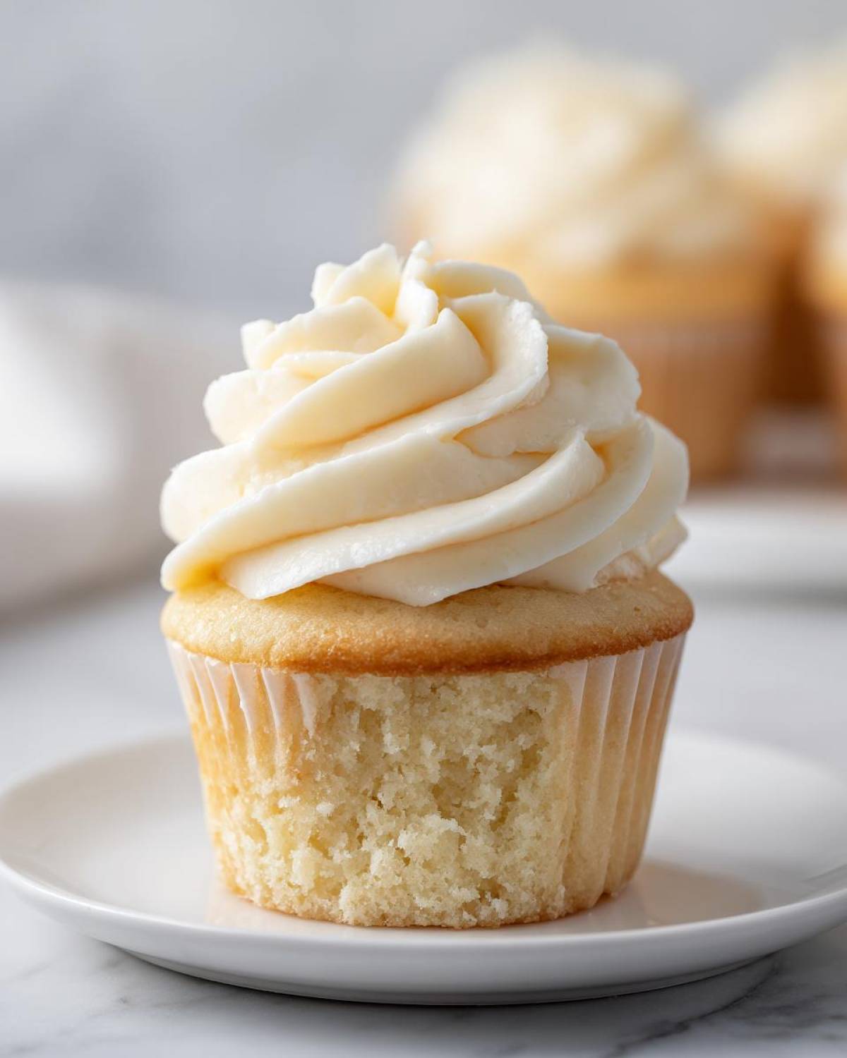 Close-up of a moist vanilla cupcakes with a tall swirl of creamy white frosting.