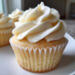 Close-up of a moist vanilla cupcake topped with a tall swirl of creamy white vanilla frosting.